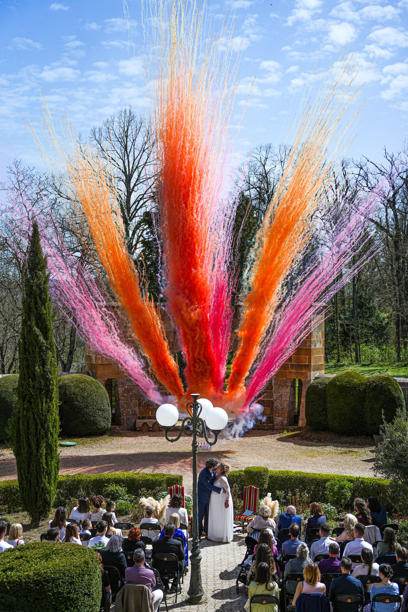 Un couple de mariés célèbre son union devant un château, sublimé par un feu d’artifice de jour coloré