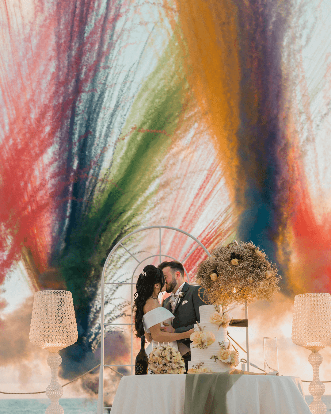 Mariage en plein air avec feu de jour multicolore et couple s’embrassant devant un décor fleuri